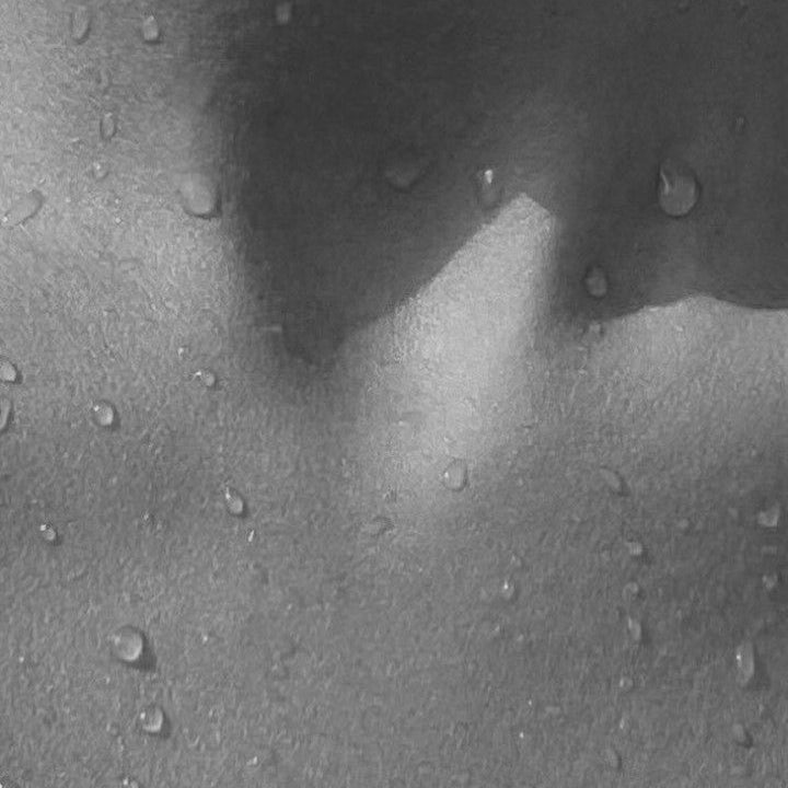 Black and white close up of water droplets on smooth skin across the collarbone and chest, evoking hydration and skin care results often associated with cosmetic treatments.